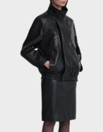 Side view of the women's oversized black lambskin bomber jacket worn closed, with hands in the pockets and the collar standing